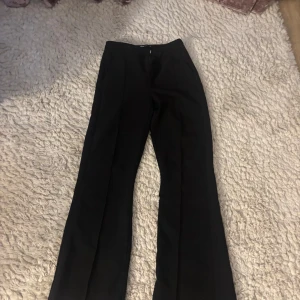 Svarta kostymbyxor - Snygga svarta kostymbyxor med medel hög midja och en elegant bootcut-stil. Perfekta för en stilren look. Byxorna har en dragkedja framtill för enkel på- och avtagning.