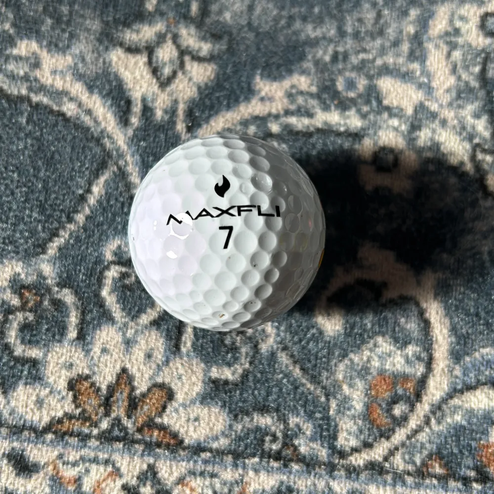 Säljer en vit golfboll från Maxfli med en unik korvbröds logga. Bollen har texten 'TOUR FIRE' och siffran 7 tryckt på sig. Perfekt för golfentusiaster som vill ha något annorlunda på banan! 🏌️♂️. Muu.