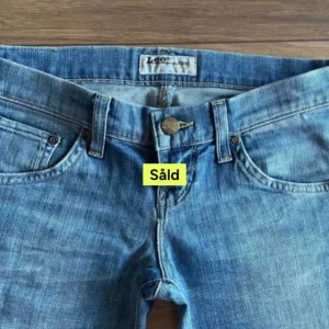 Blå bootcut jeans från Lee - Snygga blå bootcut jeans från Lee med klassisk femficksdesign och knappgylf. Perfekta för en avslappnad stil med en touch av retro. De har en bekväm passform och är tillverkade i slitstarkt denim.