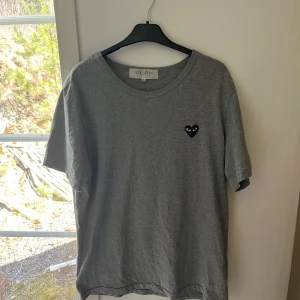 Grå t-shirt från Comme des Garçons Play - Säljer en stilren grå t-shirt från Comme des Garçons Play med det ikoniska hjärtemärket på bröstet. Tröjan sitter mer som en L. Tveka inte på att höra av er vid frågor😁