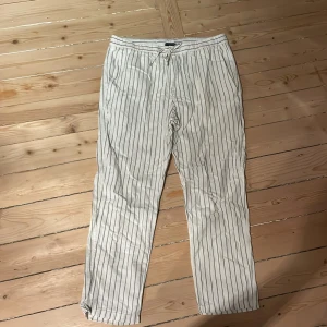 Linnebyxor från H&M - Säljer ett par bekväma och stilrena randiga byxor från H&M i storlek M. Byxorna har en midwaist passform och ger en lite fransk vibe. De är vita med svarta ränder och har en snörning i midjan för justerbar passform. De har blivit lite för små för mig och säljer nu dom. De är helt i nyskick.