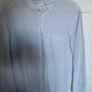 Randig skjorta från Zara - Säljer en stilren vit och blå randig skjorta från Zara. Skjortan har långa ärmar och knappar framtill samt en klassisk krage. Perfekt för en avslappnad men ändå uppklädd look.