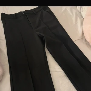 Svarta kostymbyxor - Snygga svarta kostymbyxor med en klassisk design. De har en rak passform och är perfekta för en stilren look. Byxorna har hällor för bälte och diskreta fickor på sidorna. Storlek 158. Nypris 349kr.