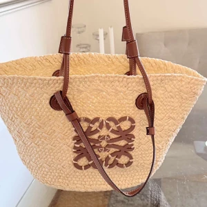 Beige shoppingväska med bruna detaljer - Snygg beige shoppingväska i flätat material med bruna läderhandtag och dekorativt mönster framtill. Perfekt för sommarens utflykter eller en dag på stan. Väskan har en rymlig insida och stilrena detaljer. Väskan är helt ny och inte använd 