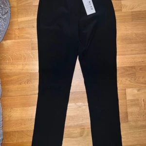 Svarta byxor från NA-KD - Snygga svarta byxor från NA-KD med en stilren design. Byxorna har en hög midja och en rak passform. De är tillverkade i ett mjukt material och har en diskret slits vid benslutet. Perfekta för en chic och elegant look. Helt nya! 