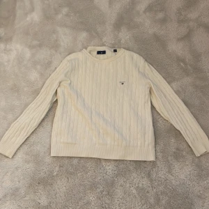 Vit stickad tröja från GANT - Säljer en stilren vit stickad tröja från GANT. Tröjan har ett klassiskt kabelstickat mönster och rund halsringning. Perfekt för kyligare dagar och ger en tidlös look. Passar barn i åldern 11-12 år.