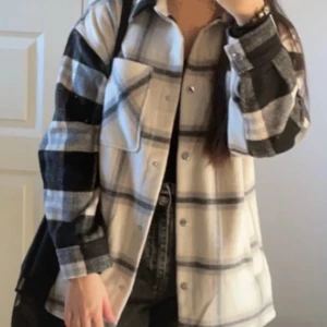 Rutig overshirt från H&M - Säljer en stilren rutig overshirt från H&M i svart och beige. Jackan har långa ärmar och knappar framtill. Perfekt för lager-på-lager-stil och ger en avslappnad look.