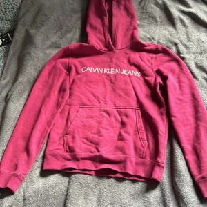 Lila/vinröd  hoodie från Calvin Klein - Säljer en snygg lila/vinröd hoodie från Calvin Klein med rosa logga på bröstet. Tröjan har en klassisk känguruficka och en bekväm huva. Storlek s.