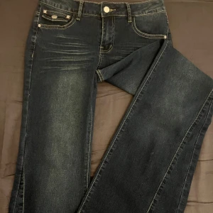 Mörkblå bootcut jeans - Snygga mörkblå bootcut jeans med klassisk femficksdesign och subtila slitningar. De har en knapp och dragkedja framtill samt bälteshällor. Perfekta för en avslappnad stil.