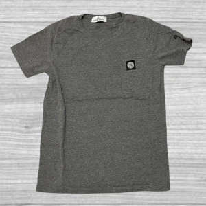 Grå t-shirt från Stone Island - Säljer en stilren grå t-shirt från Stone Island med korta ärmar och en broderad logotyp på bröstet. Perfekt för en avslappnad look. T-shirten har en rund halsringning och är tillverkad i mjukt material.