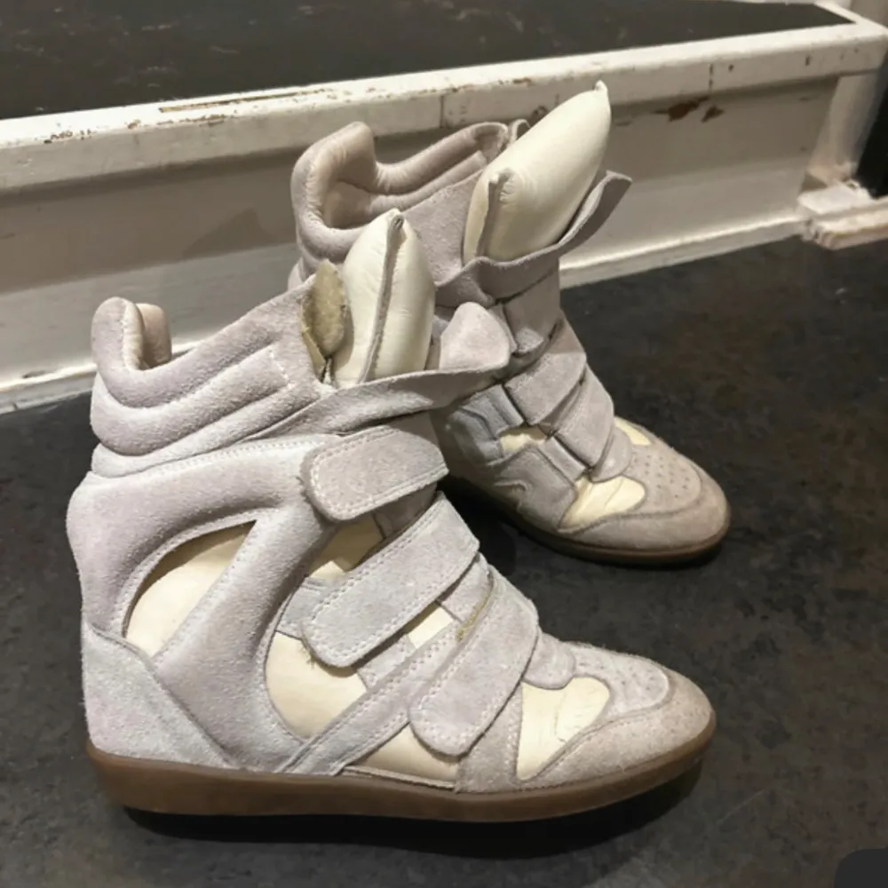 Snygga beige sneakers med kilklack och flera kardborreband. Skorna har en unik design med vadderade detaljer och perforerad tå. Perfekta för en trendig look. Lite defekter vid sidan av skorna där det har creasat. Har ej kvitto men dust bag tillkommer! (Priset är ej hugget i sten, går att pruta vid snabbt köp!). Kengät.