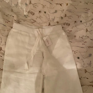 Vita linnebyxor från Aloha - Snygga vita linnebyxor från Aloha med knytband i midjan. Perfekta för en avslappnad och stilren look. Byxorna har en lös passform och är tillverkade i ett lätt och luftigt material. Köpta nu de senaste släppet så de är extra långa i benen, släpar i marken på mig som är 171! 