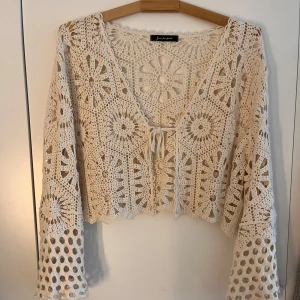 Fin beige spetskofta/bolero - Säljer en vacker beige spetskofta/bolero med ett unikt virkat mönster. Koftan har långa ärmar och en knytning framtill. Perfekt för att lägga till en bohemisk touch till din outfit. ny och oanvänd utan prislapp
