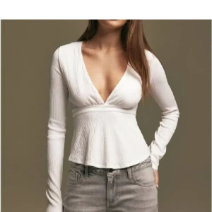 Vit ribbad topp med knyt - Säljer en stilren vit ribbad topp med v-ringning och långa ärmar. Toppen har en snygg knytning i ryggen som ger en fin detalj. Perfekt för en chic och enkel look.