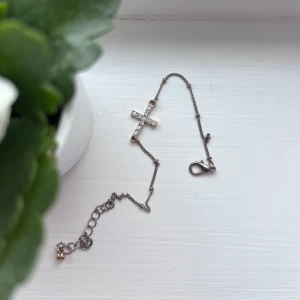 Guldarmband med kors - Elegant guldarmband med ett glittrande kors dekorerat med små stenar. Armbandet har en justerbar kedja och ett smidigt lås. Perfekt för att ge en stilren touch till din outfit. Blivit lite mörkt längst ut i kanterna. Jag lägger armbandet i plastfickan som finns på sista bilden, så det inte utsätts för skada vid leverans.