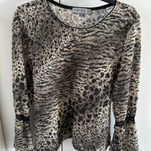 Mönstrad långärmad topp från Kriss - Snygg långärmad topp från Kriss med ett djurinspirerat mönster i beige och svart. Perfekt för att ge din outfit en unik touch. Toppen har en rund halsringning och är tillverkad i ett lätt material. Storlek M