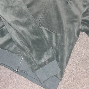 Grön hoodie från Juicy Couture - Snygg grön hoodie från Juicy Couture i mjukt material. Den har en dragkedja framtill och en broderad logga på bröstet. Perfekt för en avslappnad stil. För barn.