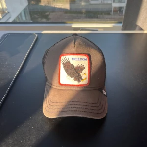 Svart keps med örn och texten 'Freedom' - Snygg svart keps med ett broderat märke på framsidan som visar en örn och texten 'Freedom'. Kepsen har ett nätmaterial på baksidan för bättre ventilation och en böjd skärm. Perfekt för en avslappnad stil.