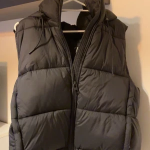 Svart väst med luva från Zara - super snygg väst från Zara. helt slutsåld!! använd vid två tillfällen och har noll tecken på användning. Står XL men sitter som en L!