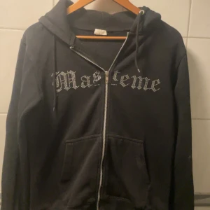 Svart hoodie från Masteme - Säljer en svart hoodie från Masteme med dragkedja och huva. På Framsidan står det Masteme i glittriga stenar och på baksidan är det Jokern som håller i ett kort. Inga av stenarna har ramlat av vad jag vet. Andvänd 1/2 ggr och köpt i slutet av 2024 så i väldigt bra skick . Tröjan är i Strl S. Köpt för 700 kr.