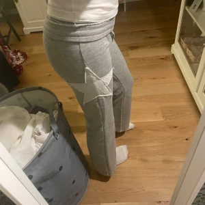 Grå mjukisbyxor med stjärndetalj🌟 - Säljer ett par grå mjukisbyxor med en vit stjärna på sidan. Byxorna har en bekväm passform med resår och snörning i midjan. Perfekta för en avslappnad stil. De är så snygga! Utsvängda💞säljer då dom är alldeles för korta för mig!