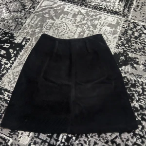 Svart kjol i manchester - Snygg svart kjol i manchester med en klassisk A-linjeform. Perfekt för att ge en stilren look. Kjolen har en enkel design utan extra detaljer.