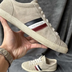 Beige sneakers från Moncler - Snygga beige sneakers från Moncler i mocka.Det är snören men dem e på tvätt.Storlek 41 passar 42.Endast skor.Så lågt pris pga en lite organe fläk snör hålen.Ge pris förslag!
