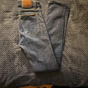 Mörkblå jeans från Nudie Jeans - Snygga mörkblå jeans från Nudie Jeans med klassisk femficksdesign och kontrasterande gul söm. Jeansen har en normal passform och är tillverkade i slitstarkt denim. Perfekta för en stilren look. Riktigt bra skick, så gott som nya🤩 Vid intresse/mer bilder är det bara att kontakta!! 🚨Snabb affär=lägre pris🚨