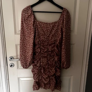 Brun blommig klänning från Shein - Säljer en söt brun klänning från Shein med vita blommor. Klänningen har långa ärmar och volangdetaljer framtill som ger en romantisk känsla. Perfekt för en dag ute eller en speciell kväll. 🌸