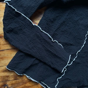 Svart tröja med vita kanter Arket - Svart tröja med vita vågiga kanter. Tröjan har långärmade ärmar och en unik textur som ger den ett stilrent utseende. Arket. Aldrig använd pga fel storlek. 