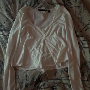 Vit långärmad topp från H&M - Säljer en söt vit långärmad topp från Vila med spetsdetaljer längs halsringningen och framtill. Toppen är använd ca 2 gånger och är i väldigt bra skick. Perfekt för sommaren💕