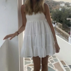 Vit klänning från Zara - Säljer en söt vit klänning från Zara med smala axelband och en luftig passform. Klänningen har en smockad överdel och volanger i kjolen som ger en romantisk känsla. Perfekt för varma sommardagar! 🌸