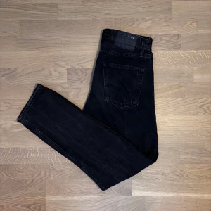 Svarta jeans från Jack and Jones - Snygga svarta jeansbyxor med en klassisk femficksdesign. De har en rak passform och är perfekta för en stilren look. Byxorna har en knapp och dragkedja framtill.
