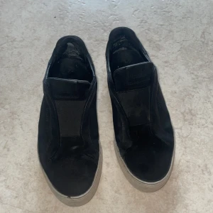 Svarta sneakers från Axel Arigato - Snygga svarta sneakers från Axel Arigato med en stilren design. Skorna har en elastisk detalj istället för snörning och en vit sula som ger en modern look. Perfekta för en avslappnad stil. OBS: ACCEPTERA INTE TILLBAKA SKICKNINGAR! 