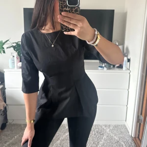 Svart blus med trekvartsärm - Snygg svart blus med trekvartsärm och figursydd passform. Perfekt för en stilren look. Blusen har en enkel design som gör den lätt att matcha med olika outfits.