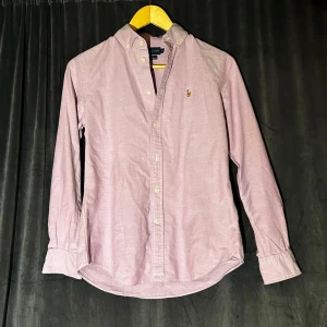 Rosa skjorta från Ralph Lauren - Säljer en stilren rosa skjorta från Ralph Lauren i slim fit. Skjortan har långa ärmar och klassiska knappar framtill. Den är broderad med den ikoniska logotypen på bröstet. Står att det är storlek 6 men säger nog att det passar en med storlek S. Kontakta gärna vid frågor! Nypris: 1600kr
