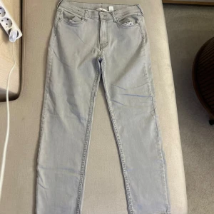 Ljusgrå jeansbyxor - Snygga ljusgrå jeansbyxor med en klassisk femficksdesign. De har en rak passform och är perfekta för en avslappnad stil. Byxorna har en dragkedja och knapp framtill.