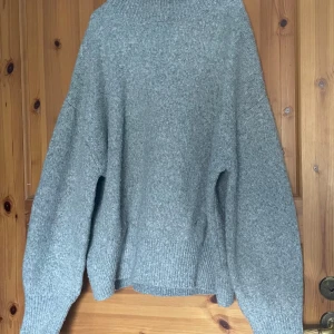 Grå stickad tröja - Mysig grå stickad tröja med polokrage och långa ärmar. Perfekt för kyliga dagar med sin avslappnade passform och ribbade detaljer vid ärmslut och nederkant.