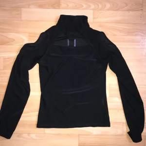 Svart polotröja från Brooker - Säljer en stilren svart polotröja från Brooker. Tröjan har långa ärmar, hög krage och öppna axlar. Passar storlek 34/36. Silverdetalj som ger en väldigt Charlies angels 2 typ av look! Även öppet över nyckelbenen.