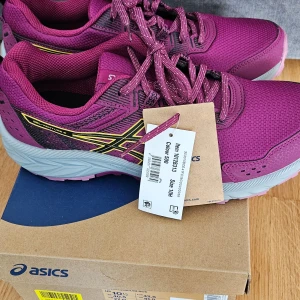 Lila löparskor från Asics - Snygga lila löparskor från Asics med svart och gul detaljering. Skorna har en robust sula med bra grepp och snörning för optimal passform. Perfekta för löpning och träning. 