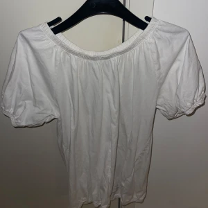 Vit blus med puffärm - Säljer en söt vit blus med korta puffärmar. Blusen har en elastisk kant vid halsen och ärmarna, vilket ger en bekväm passform. 