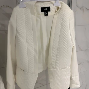 Vit Kavaj - Vit Kavaj med detaljer och fejk-fickor från H&M i storlek 36. Verkligen jättefin kavaj som knappast är använd och tyvärr inte kommit till någon användning. Passar bra till utekvällar, festliga tillfällen eller som en vår/sommar-jacka! Pris går att diskutera!! För mer info kom privat! 🤗🩷