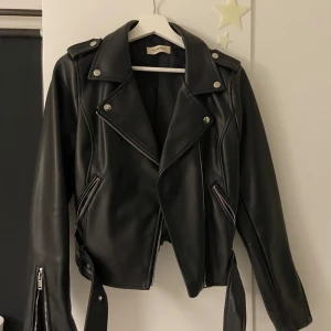 Svart skinnjacka från Glamorous - PRISET KAN DISKUTERAS VID SNABB AFFÄR!!Snygg svart skinnjacka från Glamorous med dragkedja och knappar. Jackan har en cool bikerstil med bälte i midjan och långa ärmar. Perfekt för att ge din outfit en edgy touch.