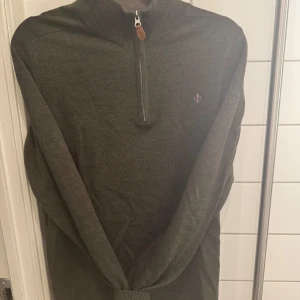 Olivgrön merinoulltröja från Morris - Säljer en stilren olivgrön tröja från Morris i 100% merinoull. Tröjan har en dragkedja vid halsen och en liten broderad logotyp på bröstet. Perfekt för kyligare dagar.