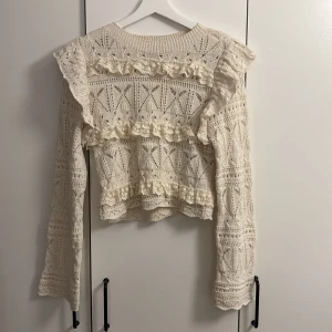 Vit stickad tröja från Zara - Säljer en vacker vit stickad tröja från Zara med fina spetsdetaljer och volanger. Tröjan har ett intrikat mönster och långa ärmar, perfekt för en stilfull look. Passar utmärkt till både vardag och speciella tillfällen. Tröjan har heller inga defekter! 