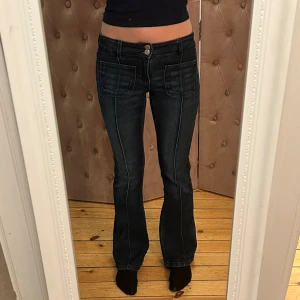 Mörkblå bootcut jeans - Snygga mörkblå bootcut jeans med hög midja och dubbla knappar fram. De har framträdande sömmar och stora fickor fram som ger en cool look.