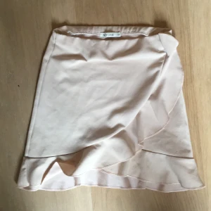 Beige omlottkjol från NLY One - Säljer en söt beige volangkjol från NLY One i storlek XS. Kjolen har en volangdetalj längst ner som ger en fin touch. Perfekt för varmare dagar och kan enkelt matchas med olika toppar. Har en liten fläck på baksidan men går bort i tvätt!