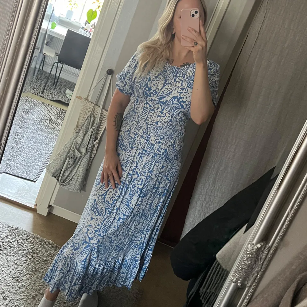 Blå/vit paisley mönstrad långklänning i mjukt och följsamt material. Går även att bära som off-shoulder. Volang nedtill och resår i ärm och midja. 100% mjuk viskos. Strl M . Mekot.
