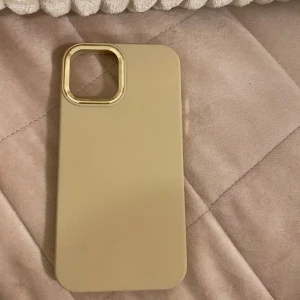  mobilskal för iPhone 12 - Snyggt och stilrent beige mobilskal med en elegant guldfärgad kant runt kameran. Perfekt för att ge din telefon ett lyxigt utseende samtidigt som den skyddas mot repor och stötar.