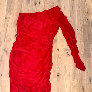 Röd oneshoulder klänning från NA-KD - Snygg röd oneshoulder klänning från NA-KD. Perfekt för en kväll ute med sin iögonfallande design. Klänningen har en åtsittande passform och är tillverkad i ett mjukt material som ger en bekväm känsla.
